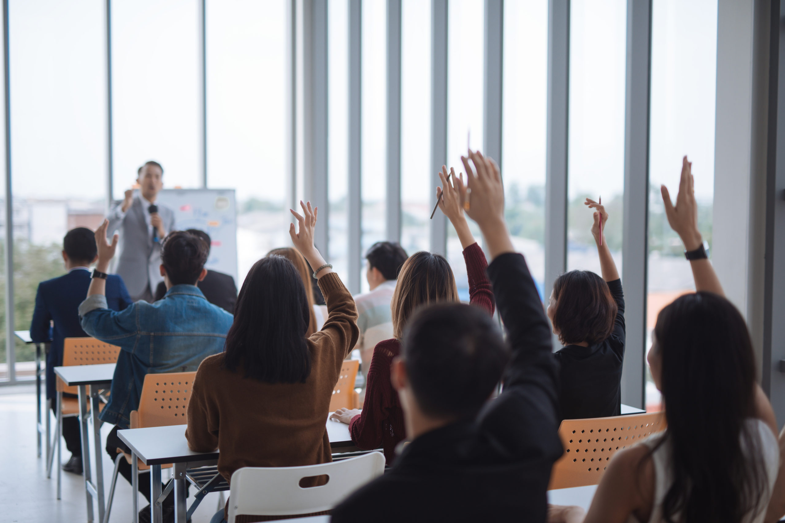 Raised up hands and arms of large group in seminar class room to agree with speaker at conference seminar meeting room